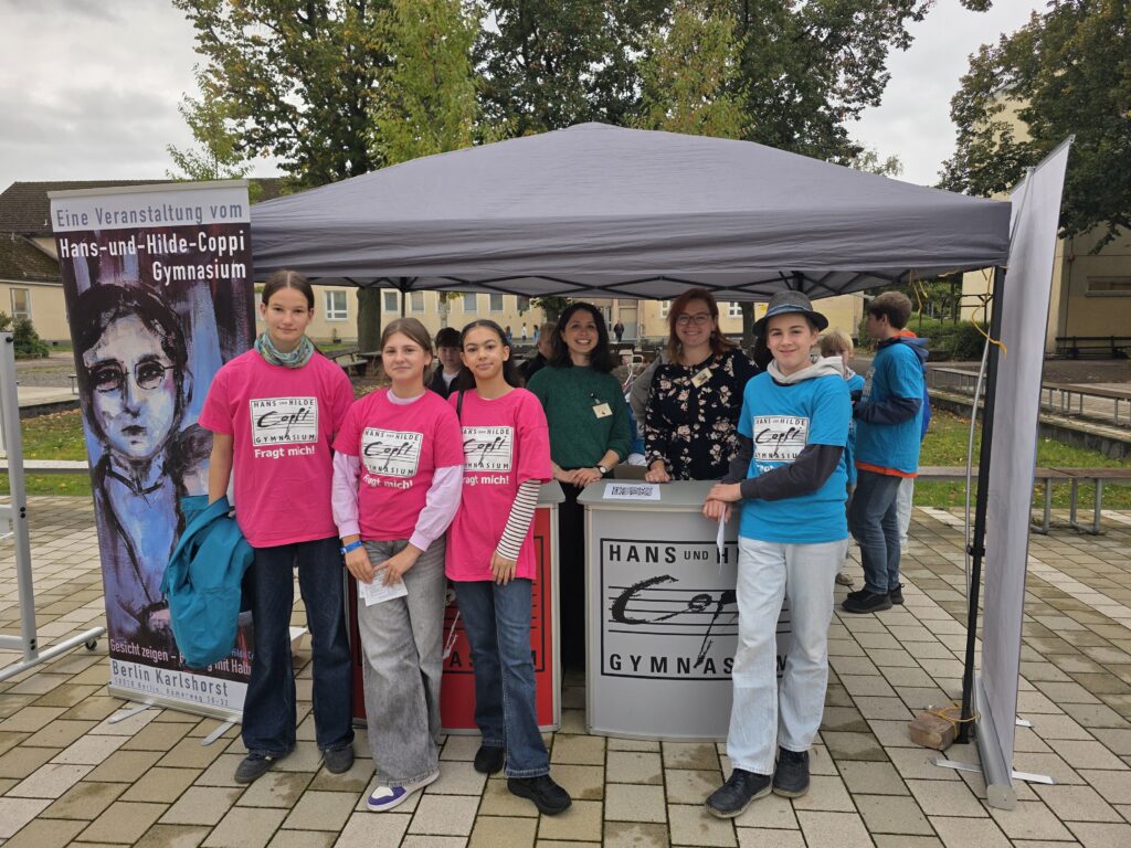 Empfangsstand beim Tag der offenen Tür mit Schülerinnen und Schülern in pinken und blauen Coppi-Shirts
